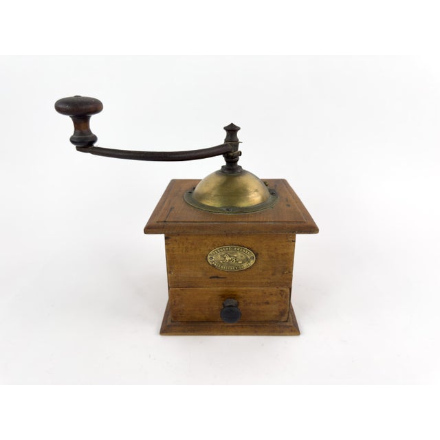 A charming early 20th-century French manual coffee grinder by Peugeot Frères, featuring a traditional wooden box, a brass-...