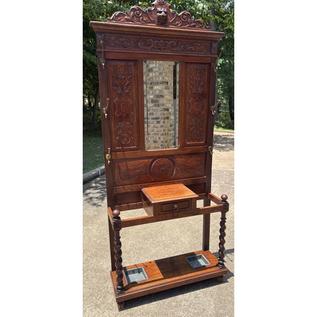 Lovely antique carved wood hall tree featuring glove box, 6 brass hooks, center mirror, two umbrella or cane stands with...