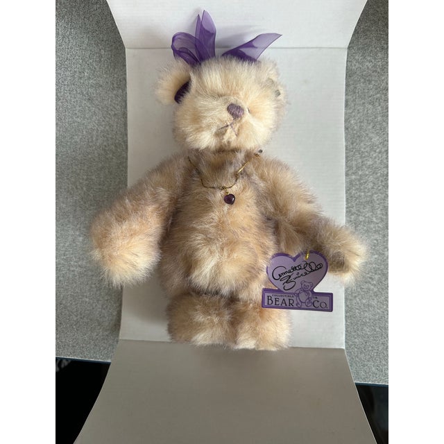 This is a collectible teddy bear from the Annette Funicello Bear Co., featuring a plush design with a purple ribbon and...
