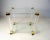 This bar cart is made of acrylic glass with two tiers and golden details. The bar cart features four wheels and two glass...