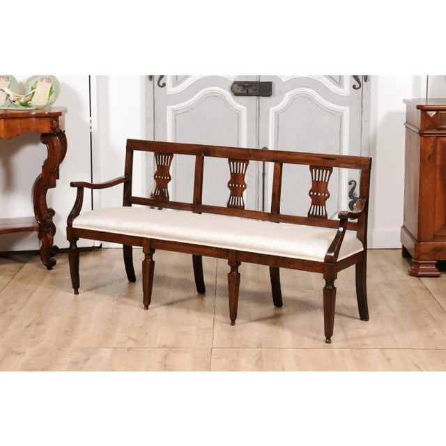 An Italian walnut three-seater bench from the 19th century with carved splats, curving open arms, tapered legs in the...