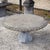 Large antique-style garden table in grey natural stone with a round tabletop and a central baluster column decorated with...