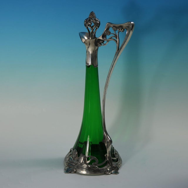 WMF green glass claret jug of stylised form, the mount depicting bathing maidens. The handle and finial modelled as a...