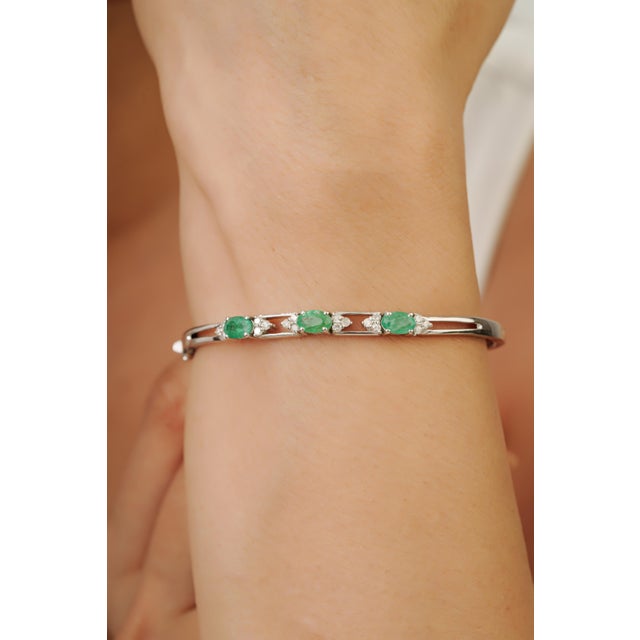 This Art Deco-style hinged bangle features 1.67 carats of oval-cut natural emeralds, each measuring approximately 4 x 6...