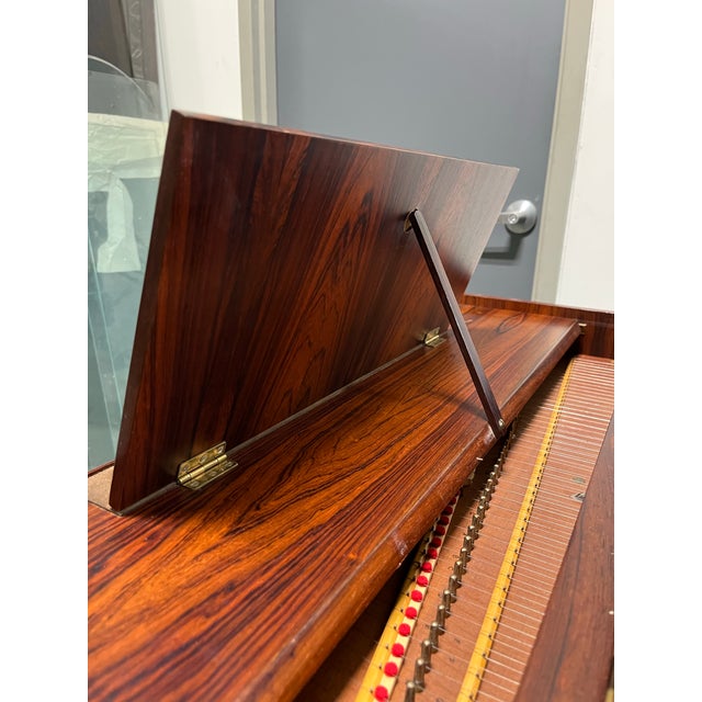 A striking mid-century modern rosewood harpsichord featuring a beautifully figured case elevated on elegant tapered legs....