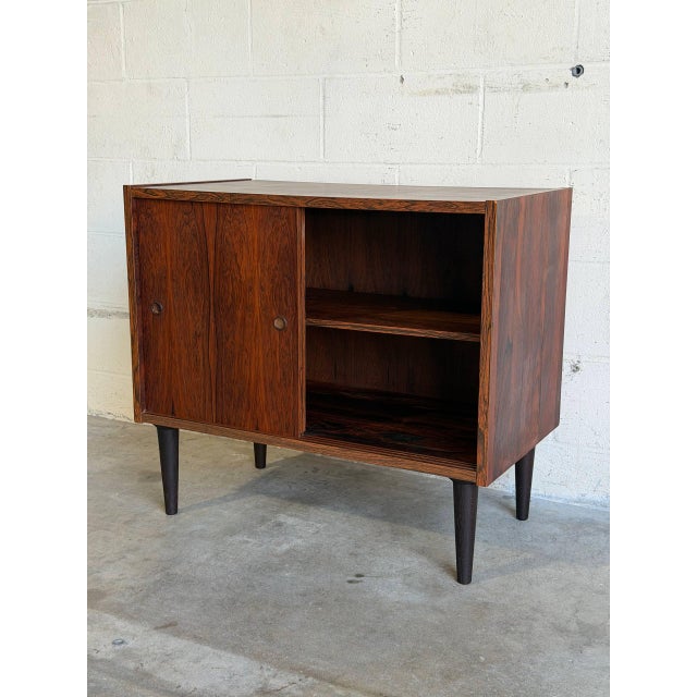 This compact storage piece features a clean rectilinear form with smooth sliding doors. Its minimalist silhouette...