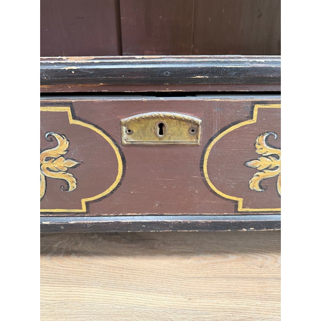 This antique bookcase features a rich, dark-colored finish adorned with intricate gold-colored stencil work along the top...
