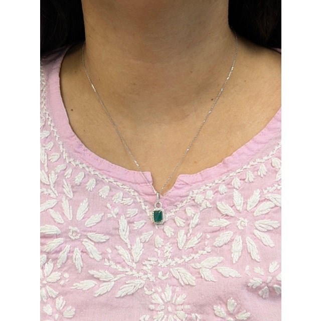 An emerald glows with green brilliance at the heart of this emerald cut pendant, framed by a trail of brilliant natural...