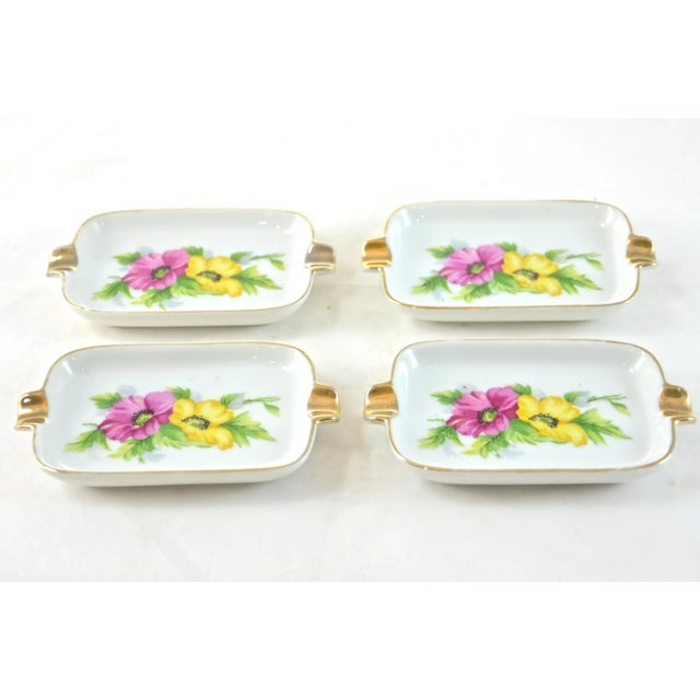 Set of four porcelain ashtrays adorned with a spring floral pattern and gilt accents. Marked “Japan.” Light wear.