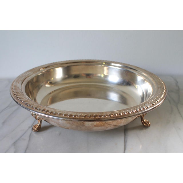Vintage footed silverplate serving bowl features a classic round shape, an ornate rim, and decorative claw and shell feet....
