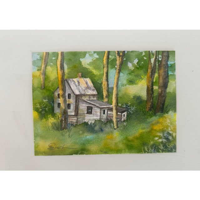 A charming woodland cottage nestled among tall sunlit trees, this original watercolor captures the quiet magic of a hidden...