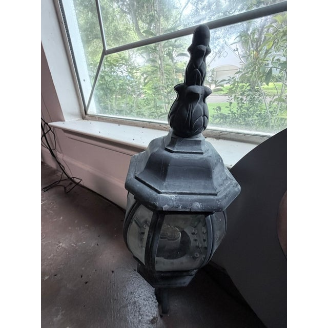 A classic heavy cast-iron wall lantern sconce with a round faceted glass globe and elaborate scrollwork mounting bracket....