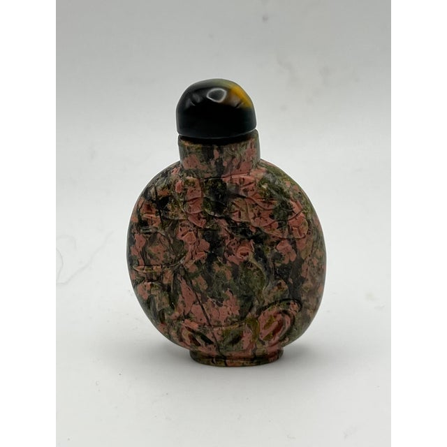 The small flattened round snuff bottle with a small raised oval foot is made of Unakite, a semi-precious stone composed of...