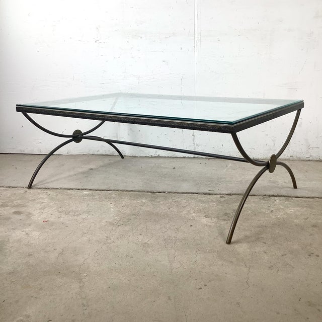 A sophisticated sculptural coffee table featuring a hand-forged style patinated iron base supporting a thick beveled glass...