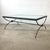 A sophisticated sculptural coffee table featuring a hand-forged style patinated iron base supporting a thick beveled glass...