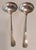 Two small sterling silver ladles with plain, gently widening handles and shallow rounded bowls. Each handle bears an...
