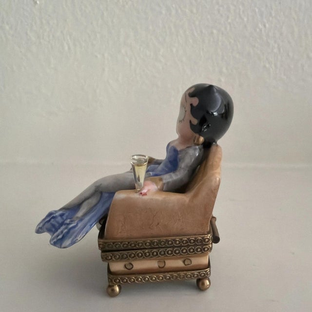 This rare Limoges trinket box features Betty Boop in an armchair with a champagne bottle, making it a unique and eye-...