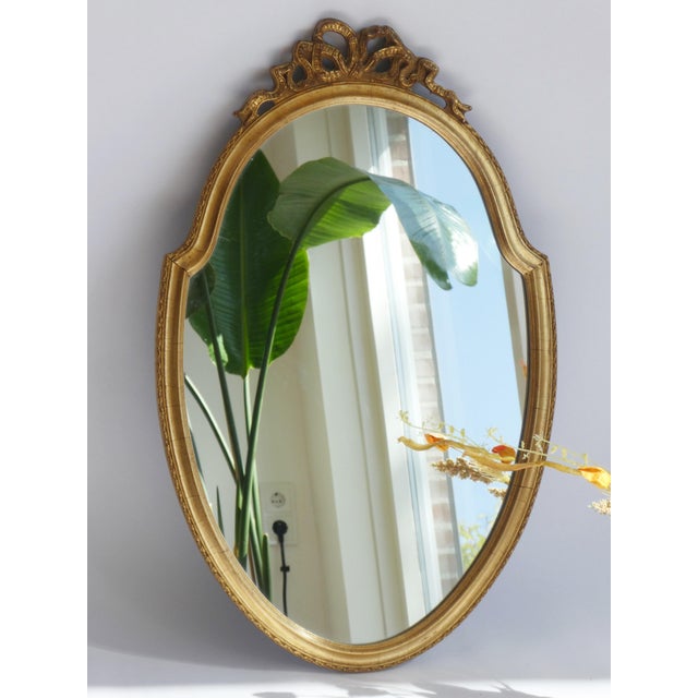 A vintage French gold gilt mirror. The beautiful mirror has an ornate frame with a bow on the top. It has a nice oval...