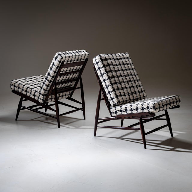 A pair of Italian lounge chairs from the 1950s, featuring a dark-stained wooden frame with tapered legs and cross...