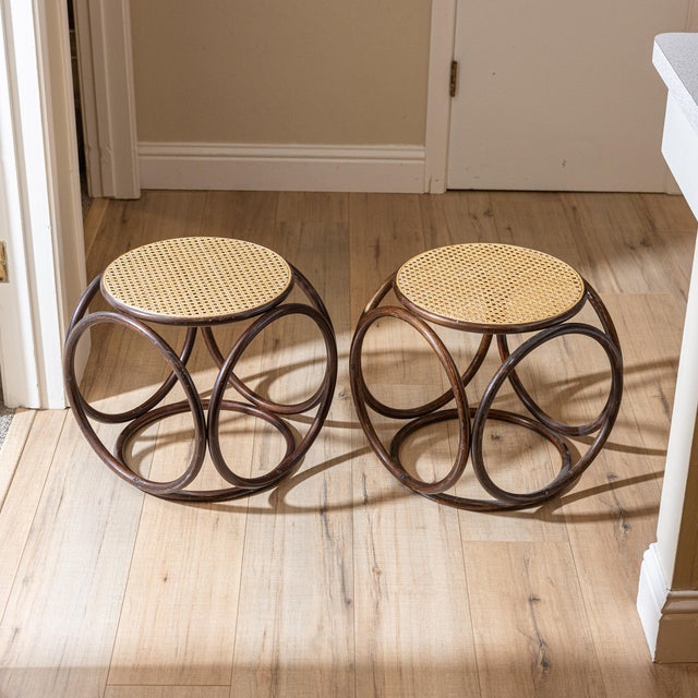 Sculptural pair of vintage bent rattan stools or side tables featuring a striking circular framework and woven cane tops....
