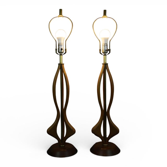 This striking pair of vintage 1960s Mid Century Modern table lamps features sculpted walnut bodies in the classic Modeline...