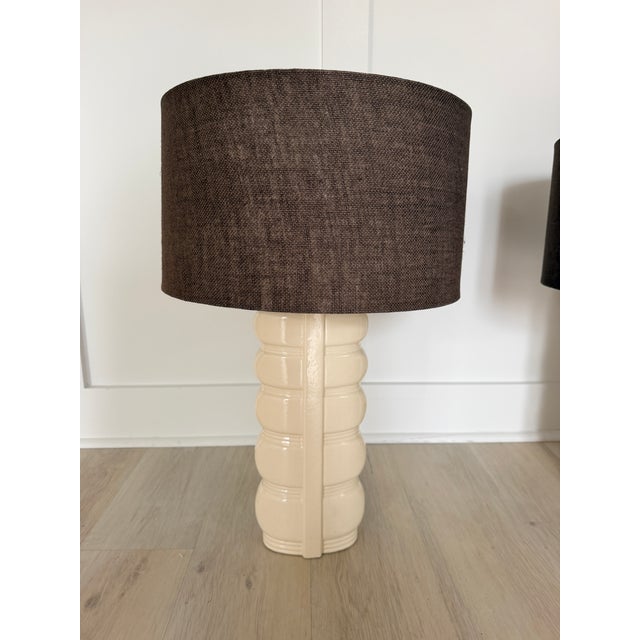 A striking pair of vintage mid-century modern ceramic table lamps featuring sculptural cream glazed bases paired with rich...