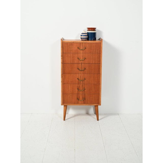 Small Scandinavian teak chest of drawers with brass handles, a raised profile, and slender proportions for a decorative...