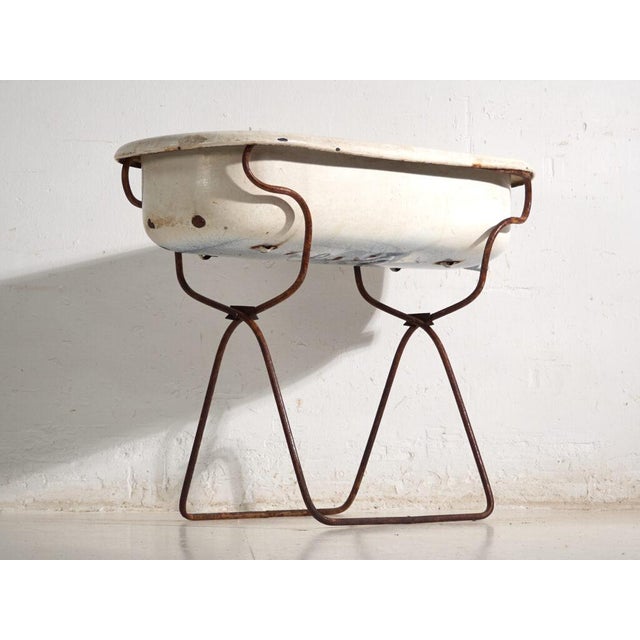 This antique bathtub in enamelled iron rests on a folding stand of bent iron tube. Originates from Central Europe, from...