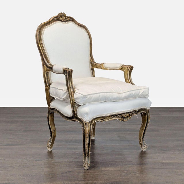 This beautiful vintage armchair features a classic wood frame with ornate gold trim and soft white upholstery. The...