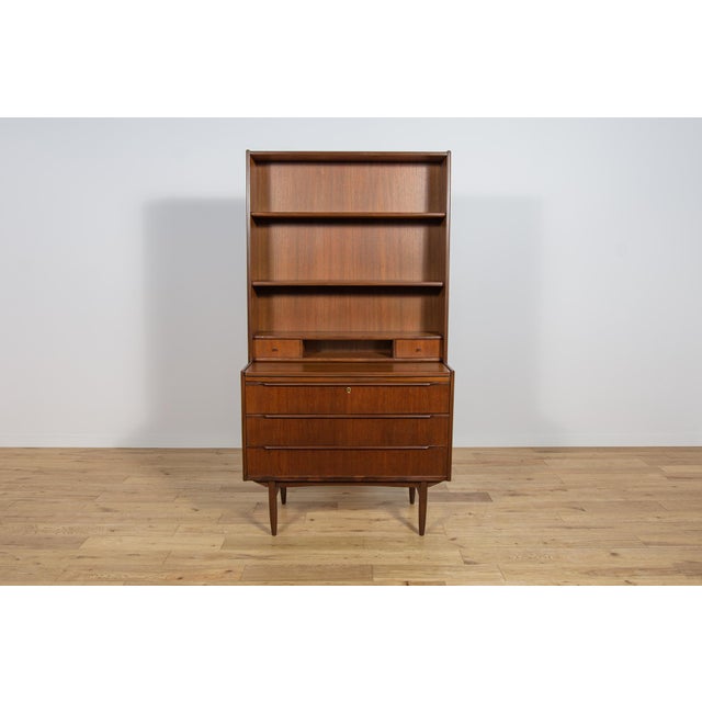 This mid century shelf in teak was manufactured in the Denmark the 1960s. This mid century shelf has 3 shelves and 4 small...