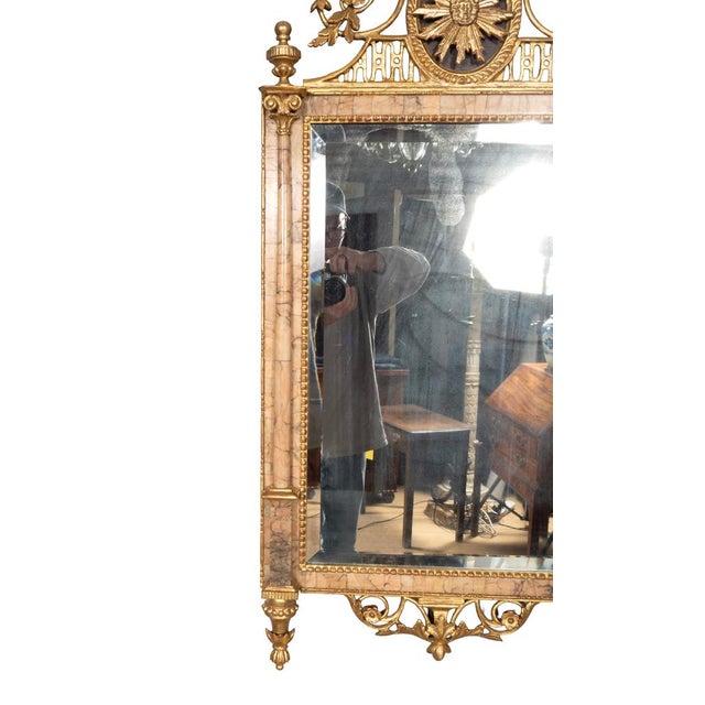 With elaborate crest with floral finial and central sunburst over a mirror surrounded by pink marble with columns....