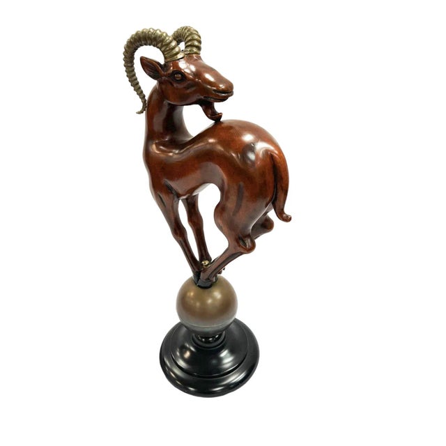 A Mid-Century Wooden Ram Sculpture. The sculpture is mounted on a brass sphere featuring brass horns. The brass horns add...