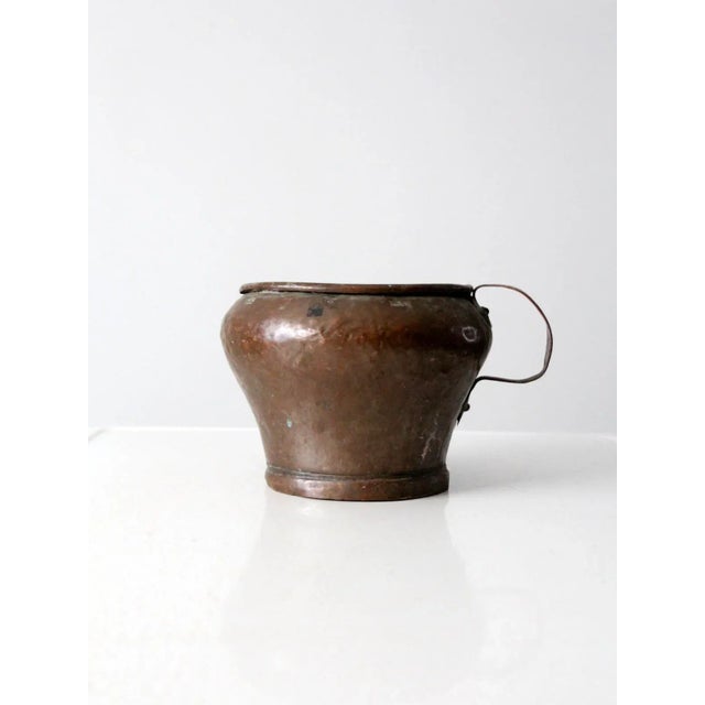 This is an antique spoutless copper pitcher featuring a hammered body, a copper handle, and a gracefully curled rim. The...