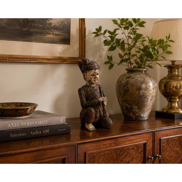This finely detailed hand-carved Chinese wooden figural sculpture depicts a seated musician holding a trumpet-style wind...