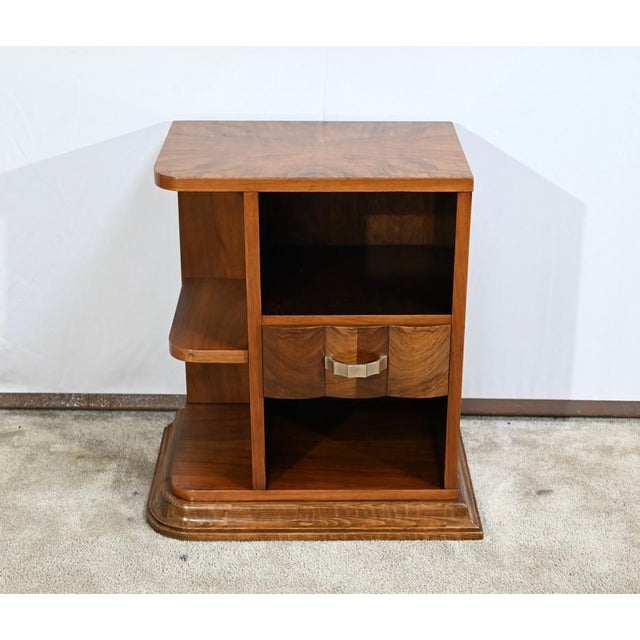 This small bedside table, in solid and plated walnut, opens with a drawer, with a triple movement facade, with chrome...