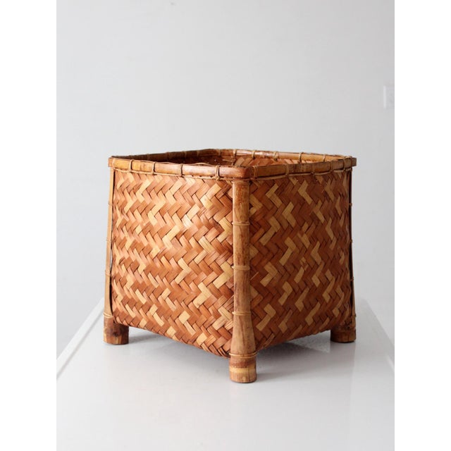 A vintage 1970s woven bamboo storage basket featuring an intricate geometric herringbone pattern in alternating shades of...