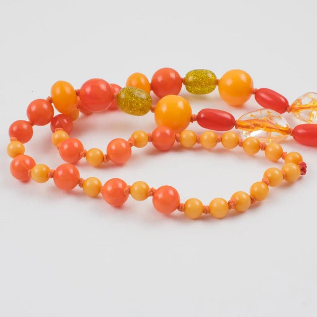 This colorful extra-long Bakelite and Lucite necklace features assorted beads in various carved shapes: round, tomato, and...