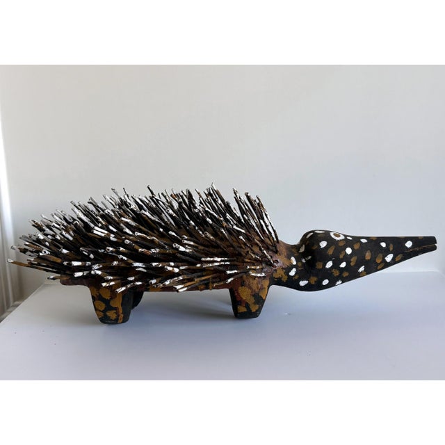 An echidna sculpture carved from wood, supplemented with found branches and splash painted with ocher pigment by...