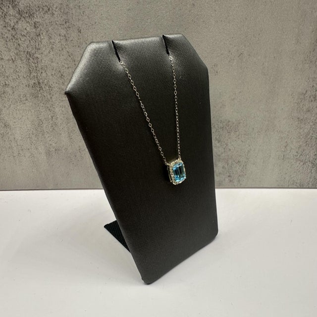 This elegant topaz and diamond necklace in 10kt yellow gold features a vibrant emerald cut blue topaz measuring...