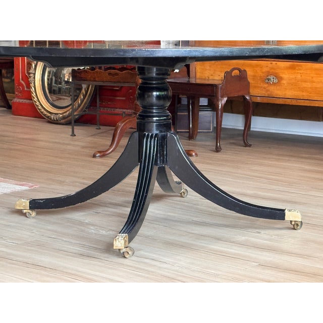 A large round ebonized dining table with a bold gilt Greek key border running the full circumference of the top and a fine...