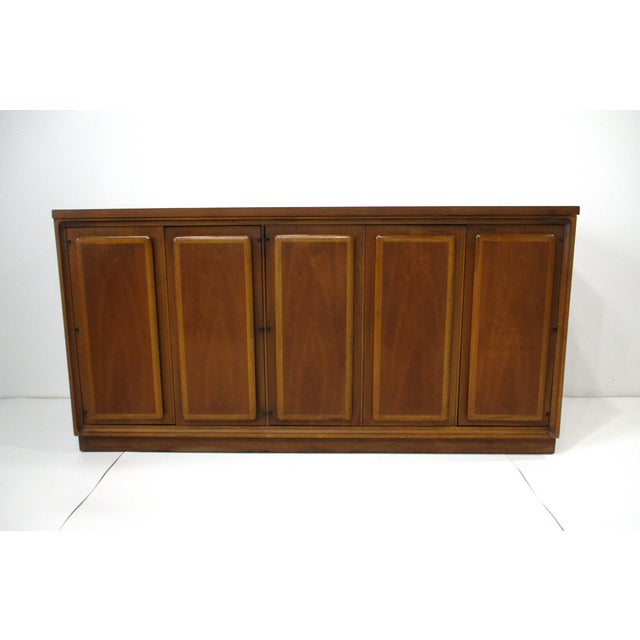 A walnut Mid Century credenza / server with two toned door edges which give the piece a unique aesthetic . To the left...