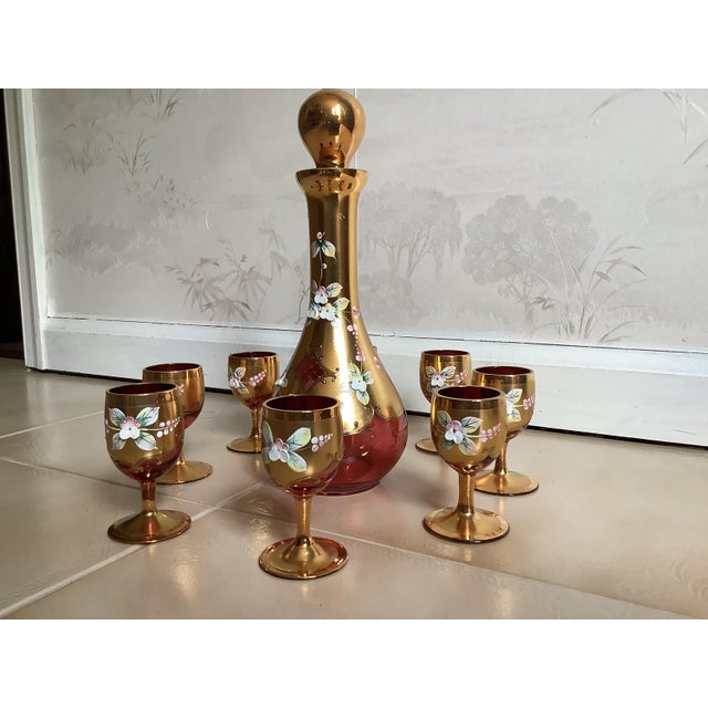 Murano Ruby red glass decanter and 8 glass cups featuring 24k gold gilt and hand painted white enamel flowers. I bought...