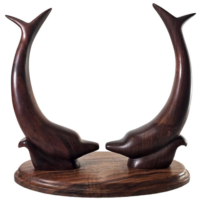 Two dolphins rise from walnut, their forms fluid, arched in mirrored grace. Hand-carved with precision, the wood carries...