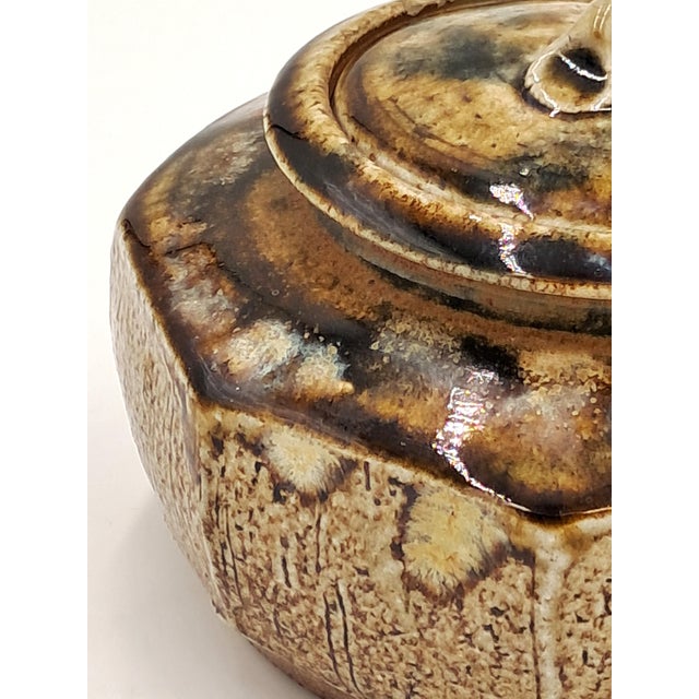 This stunning hand-thrown studio lidded jar is in the shape of an octagon and features a rough-hewn texture with a brown...