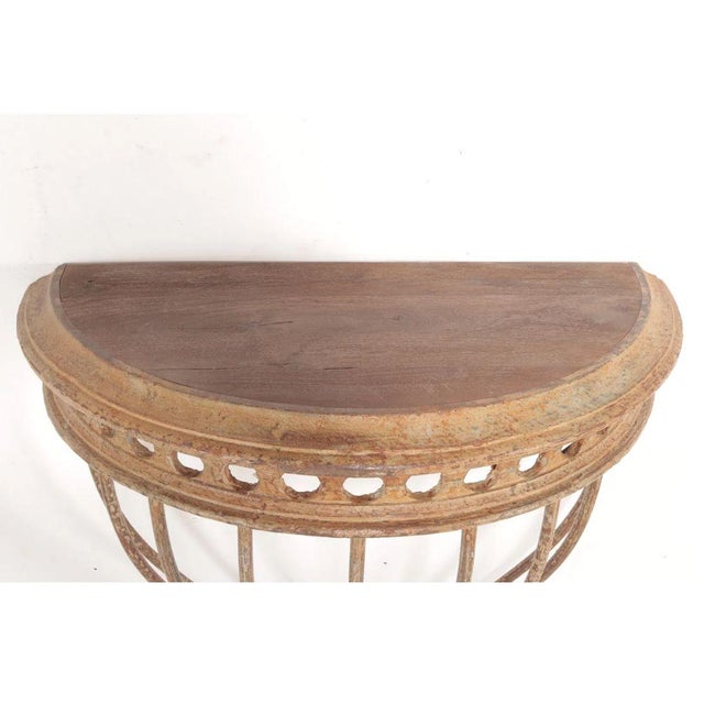 A vintage demi-lune console table featuring a gracefully curved wrought iron base supporting an inset teak wood top. The...