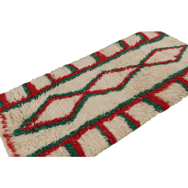 Hand-knotted in wool circa 1950-1960, this 3x7 vintage Moroccan runner rug with geometric patterns in red and green, hails...