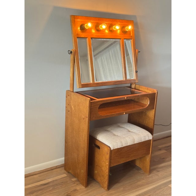 A Scandinavian-inspired mid-century oak vanity featuring a distinctive tri-fold mirror and integrated light, produced in...