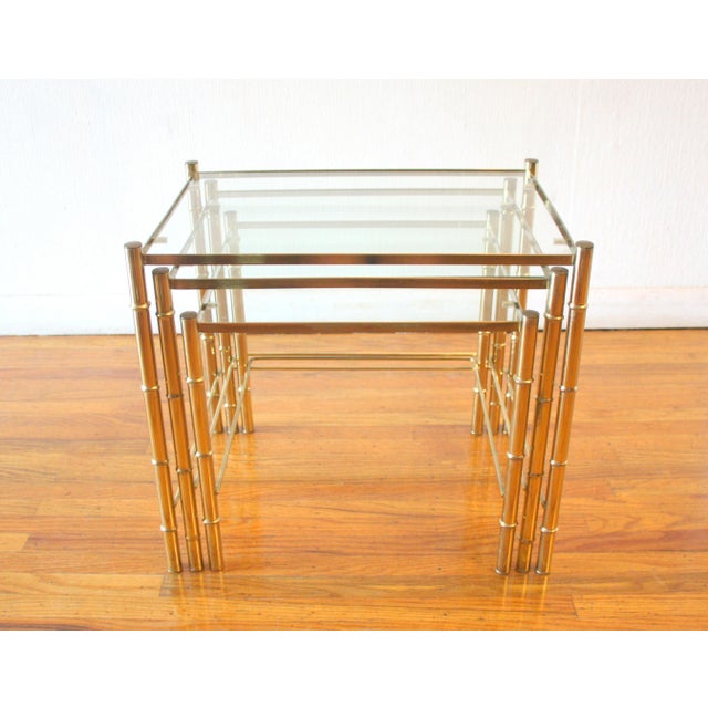 This is a set of 3 mid century modern brass and glass Hollywood Regency style nesting tables with a faux bamboo design....