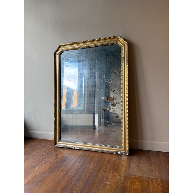 French giltwood mirror featuring a classic rectangular form with softly angled corners at the top, beaded inner molding,...