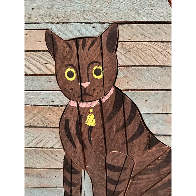 A cat sits framed by a pair of drawn-back curtains, its yellow eyes wide and watchful, a small pendant hanging from its...